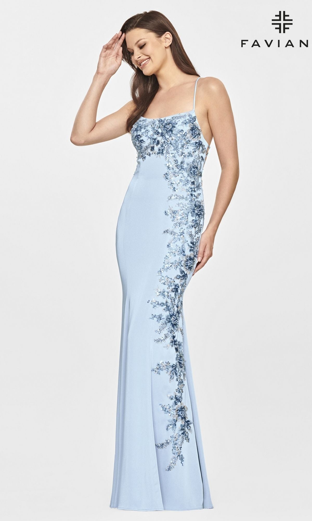 A woman models the Faviana Open-Back Long Tight Prom Dress with Lace, a light blue sequin gown featuring floral embellishments, as she poses against a plain background with the